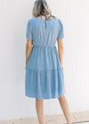 Back view of Model wearing a blue and white gingham tiered dress with an elastic waistband. 