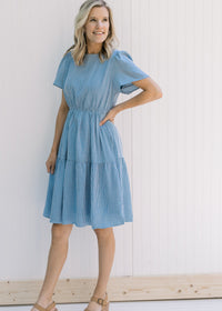 Model wearing heels with a short sleeve, blue and white gingham tiered dress with an elastic waist.