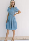 Model wearing heels with a short sleeve, blue and white gingham tiered dress with an elastic waist.
