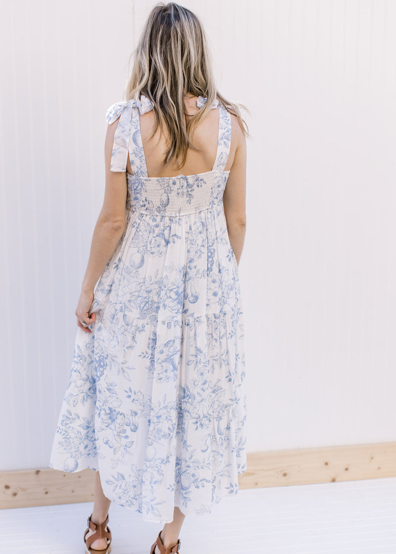 Back view of Model wearing a white tiered midi with blue floral, tie straps and a square neck