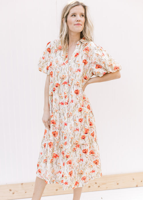 Model wearing a cream dress with red flowers, a button front and bubble short sleeves.