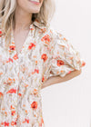 Close up of a cream v-neck dress with red flowers, a collar and bubble short sleeves. 