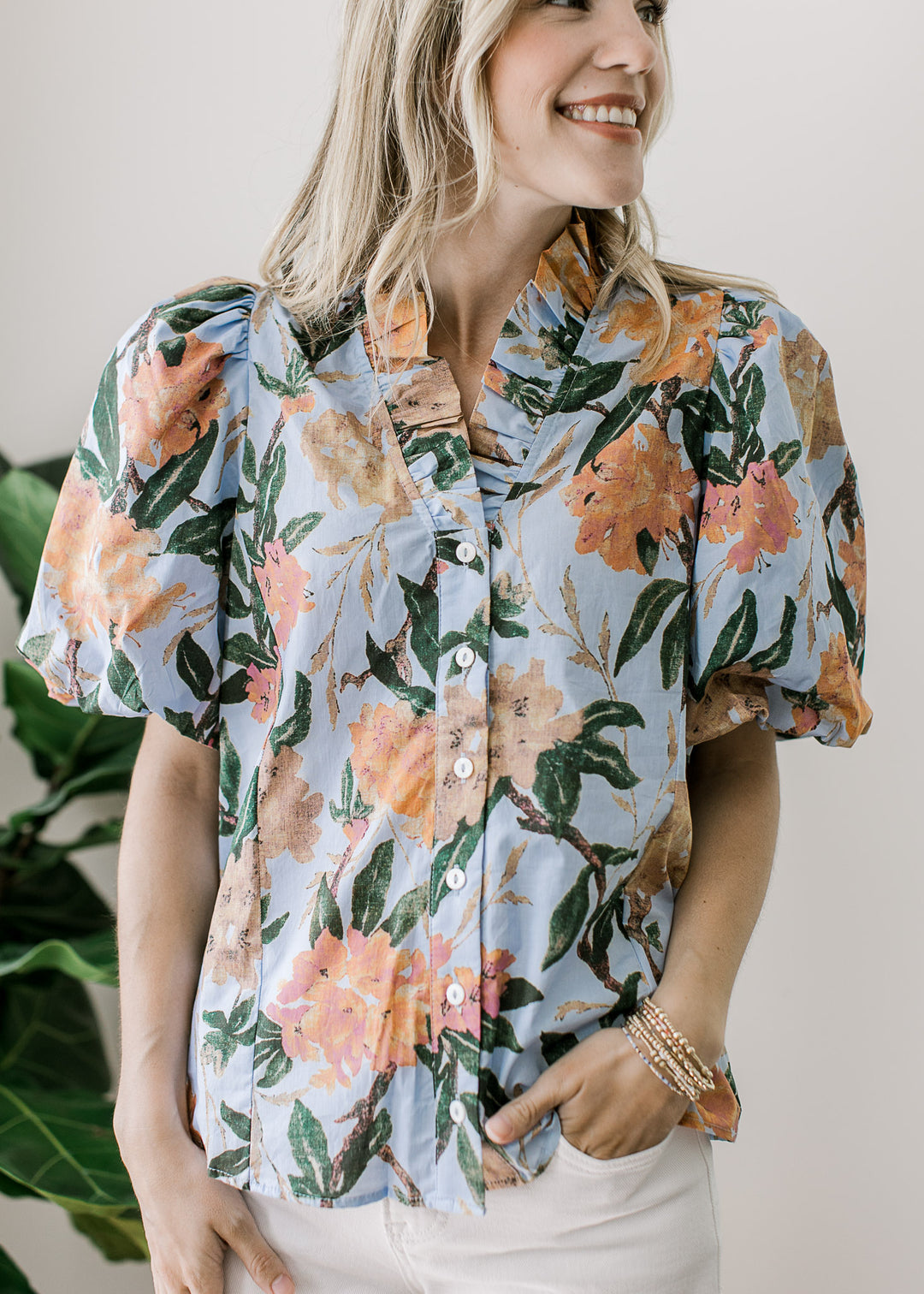 Model wearing a pale blue button up with coral and tan floral, puff short sleeves and ruffle v-neck.