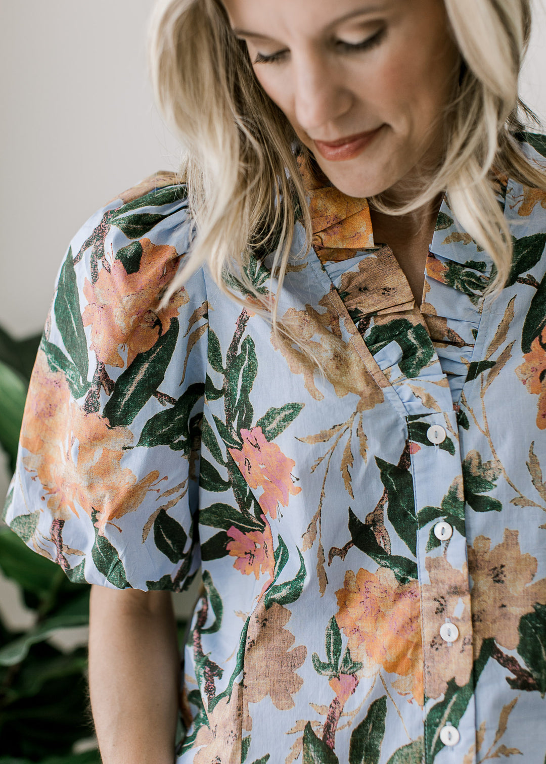 Close up of v-neck with ruffle and puff short sleeves on a pale blue top with floral pattern. 
