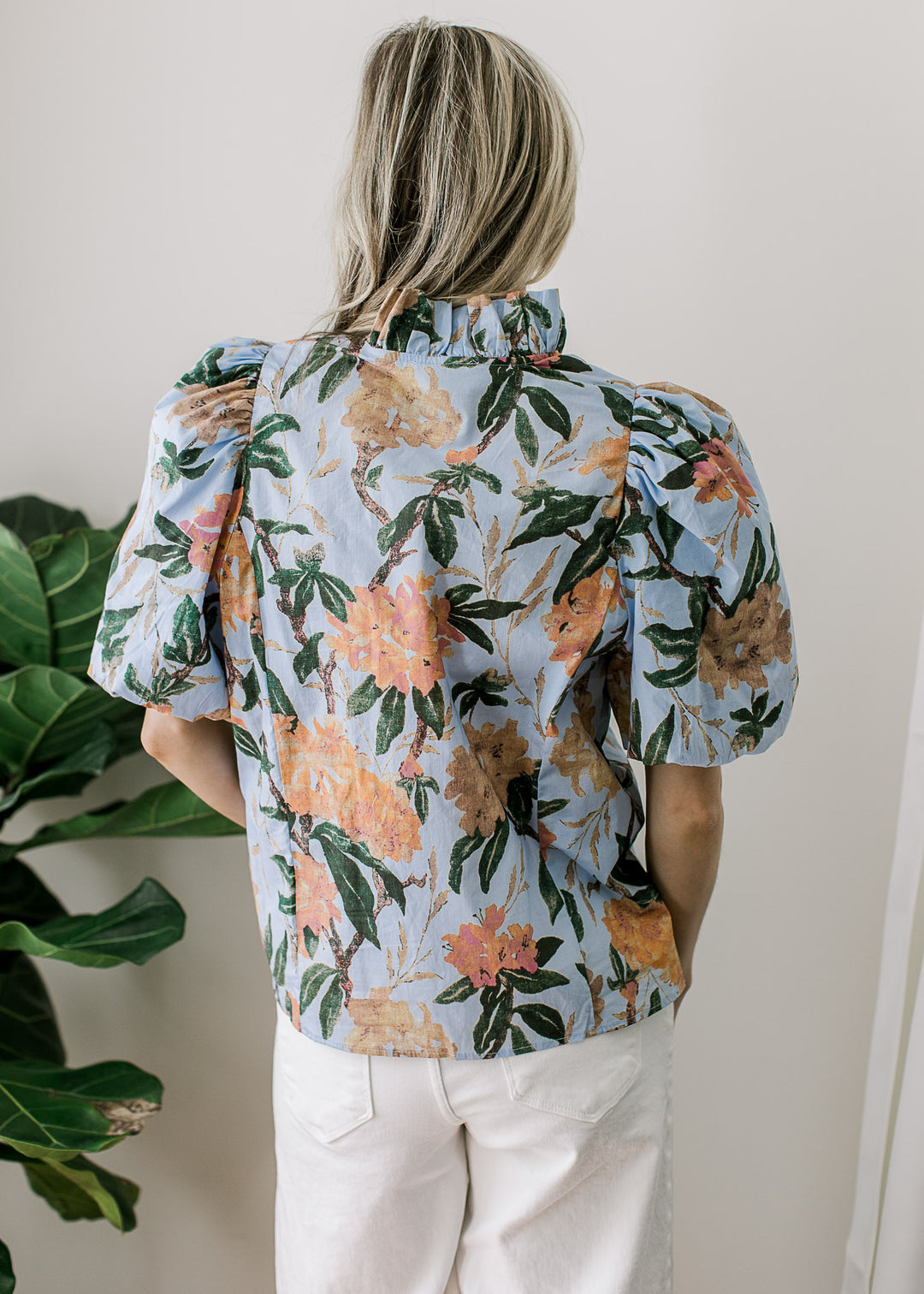 Back view of Model wearing a pale blue top with coral and tan floral and puff short sleeves. 