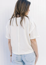 Back view of Model wearing a cream ribbed top with cuffed short sleeves and a round neck.