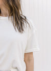 Close up of cuffed short sleeves and ribbed detail on a cream top with a round neckline.