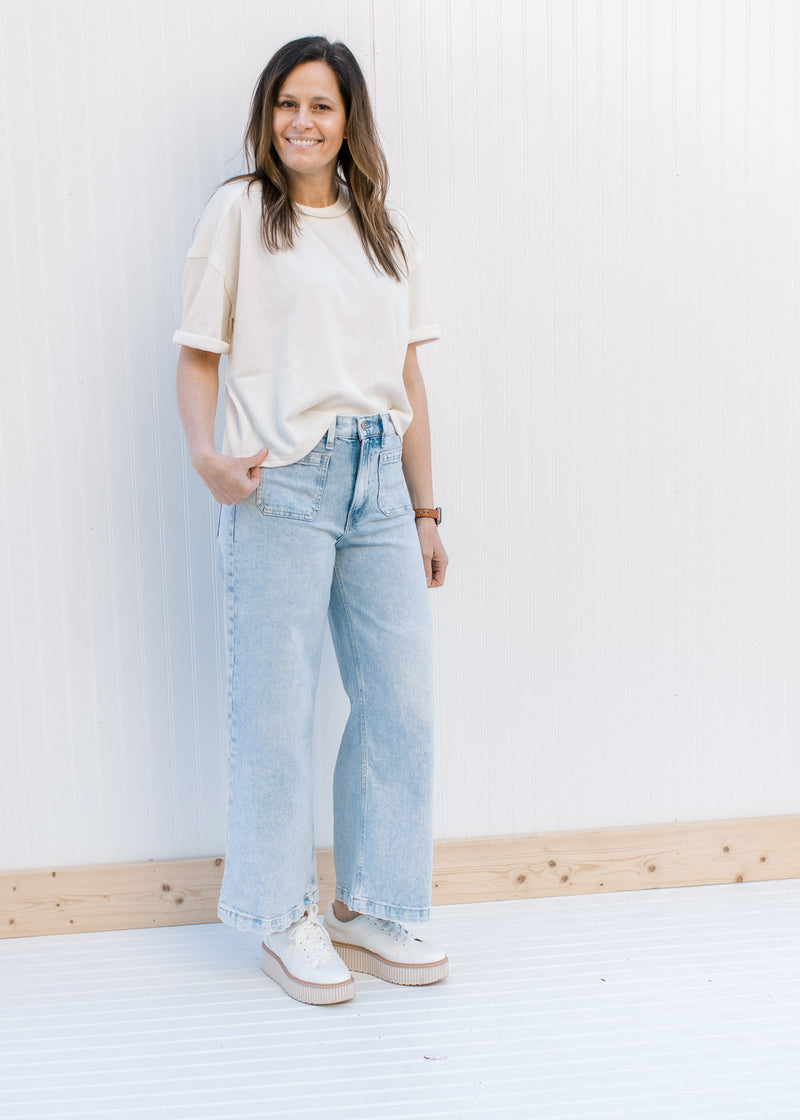 Model wearing jeans, sneakers and a cream ribbed top with cuffed short sleeves and a round neck.