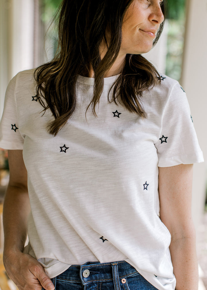 Model wearing a white short sleeve top with navy embroidered stars and a crew neck. 