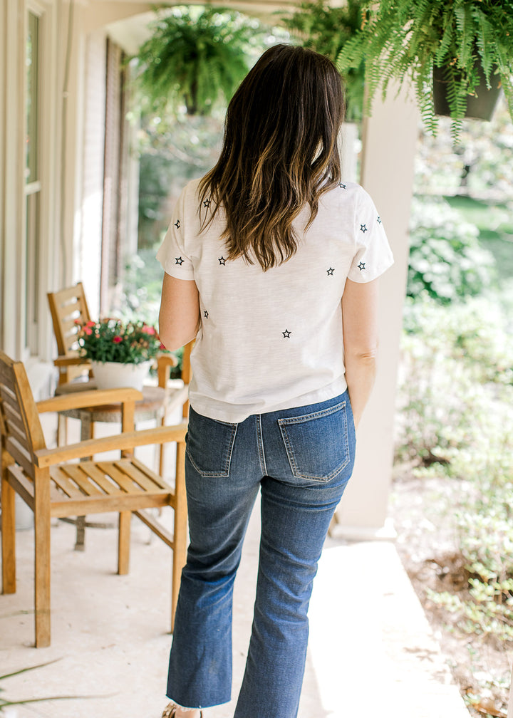 Back view of Model wearing a white short sleeve top with navy embroidered stars and a crew neck. 