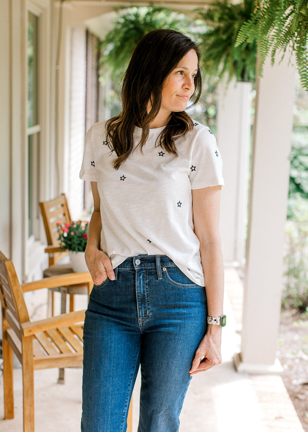 Model wearing jeans and a white short sleeve top with navy embroidered stars and a crew neck. 