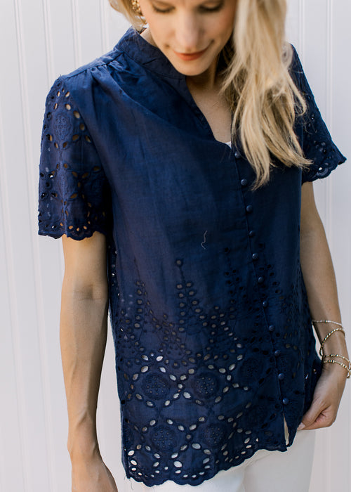 Model wearing a navy button up top with eyelet detail and scalloped short sleeves and hem.