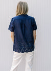 Back of Model wearing a navy button up top with eyelet detail and scalloped short sleeves and hem.