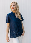 Model wearing white pants with a navy top with eyelet detail and scalloped short sleeves and hem.