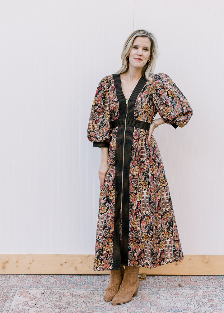 Model wearing a black midi with fall floral, 3/4 bubble sleeves, gold zip front and long sleeves.