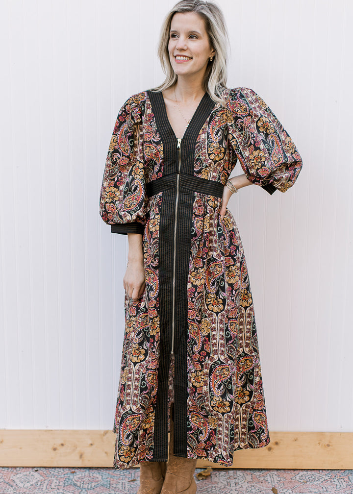 Model wearing boots and a black midi with warm fall floral, 3/4 bubble sleeves and a gold zip front.