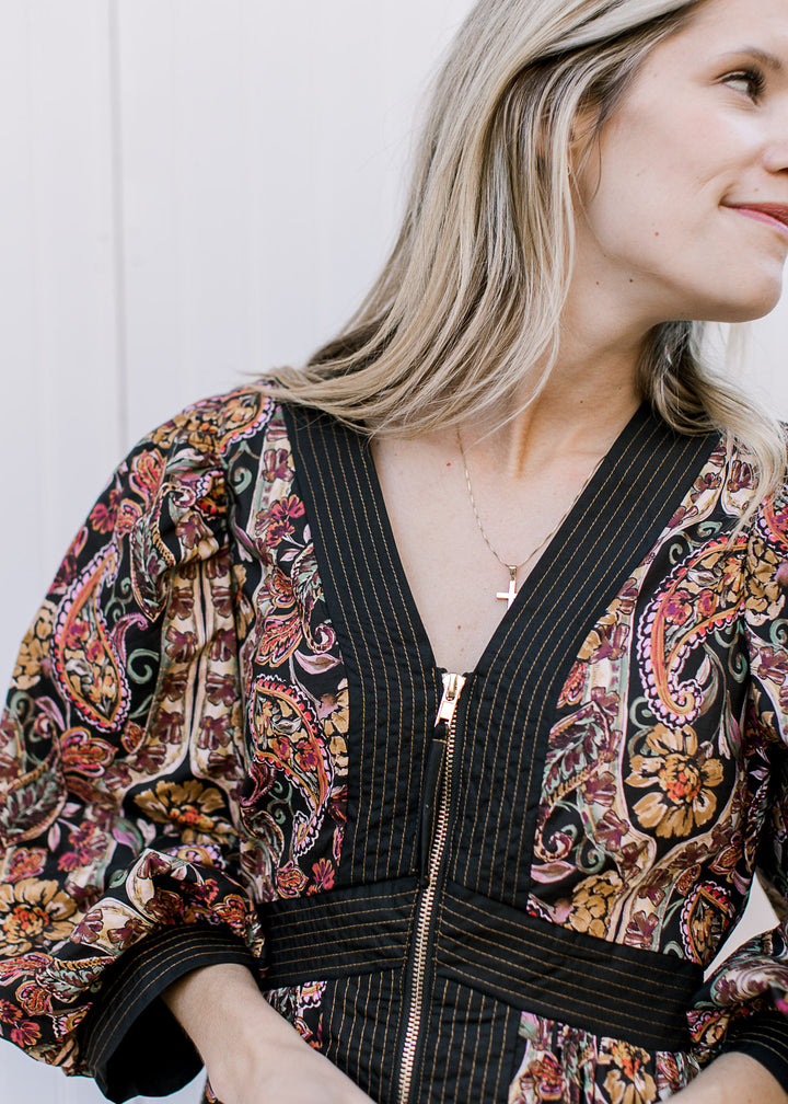 Close up of v-neck and gold zipper on a black midi with warm fall floral and black line detailing. 