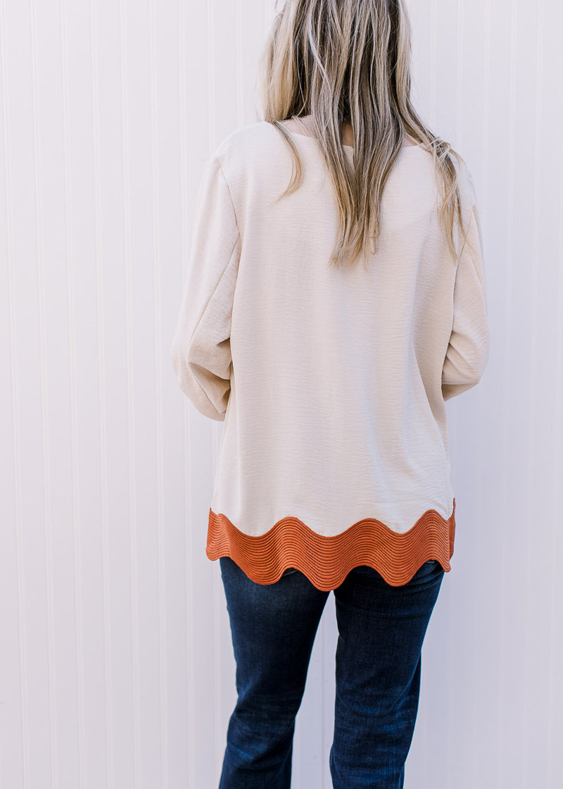 Back view of model wearing a cream top with rust ric-rac hem, 3/4 sleeves and a round neck.