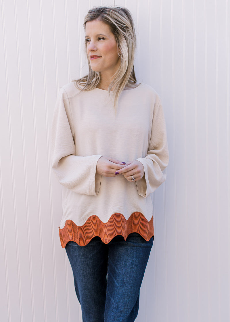 Model wearing jeans and a cream top with rust ric-rac hem, keyhole closure and a round neck.