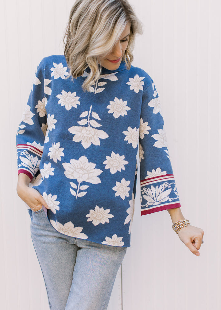 Model wearing a steel blue sweater with cream and tan floral, mock neck and 3/4 bell sleeves.