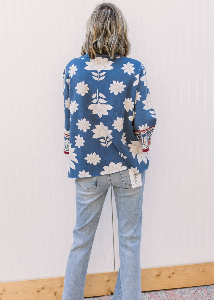 Back view of Model wearing a steel blue sweater with cream and tan floral and 3/4 bell sleeves.