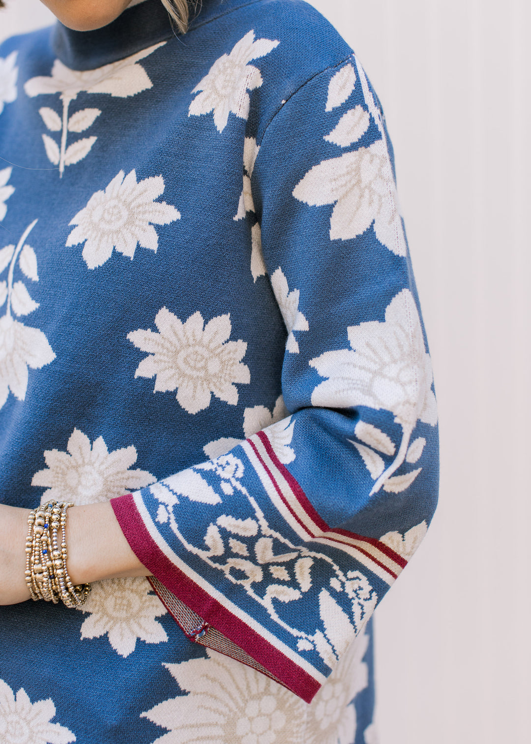 Close up of 3/4 bell sleeves with maroon detailing on a steel blue sweater with cream floral.