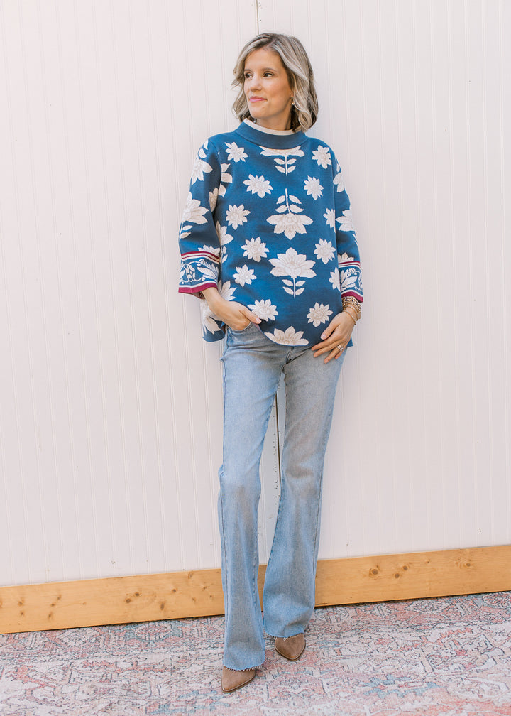 Model wearing jeans and a steel blue sweater with cream and tan floral and 3/4 bell sleeves.