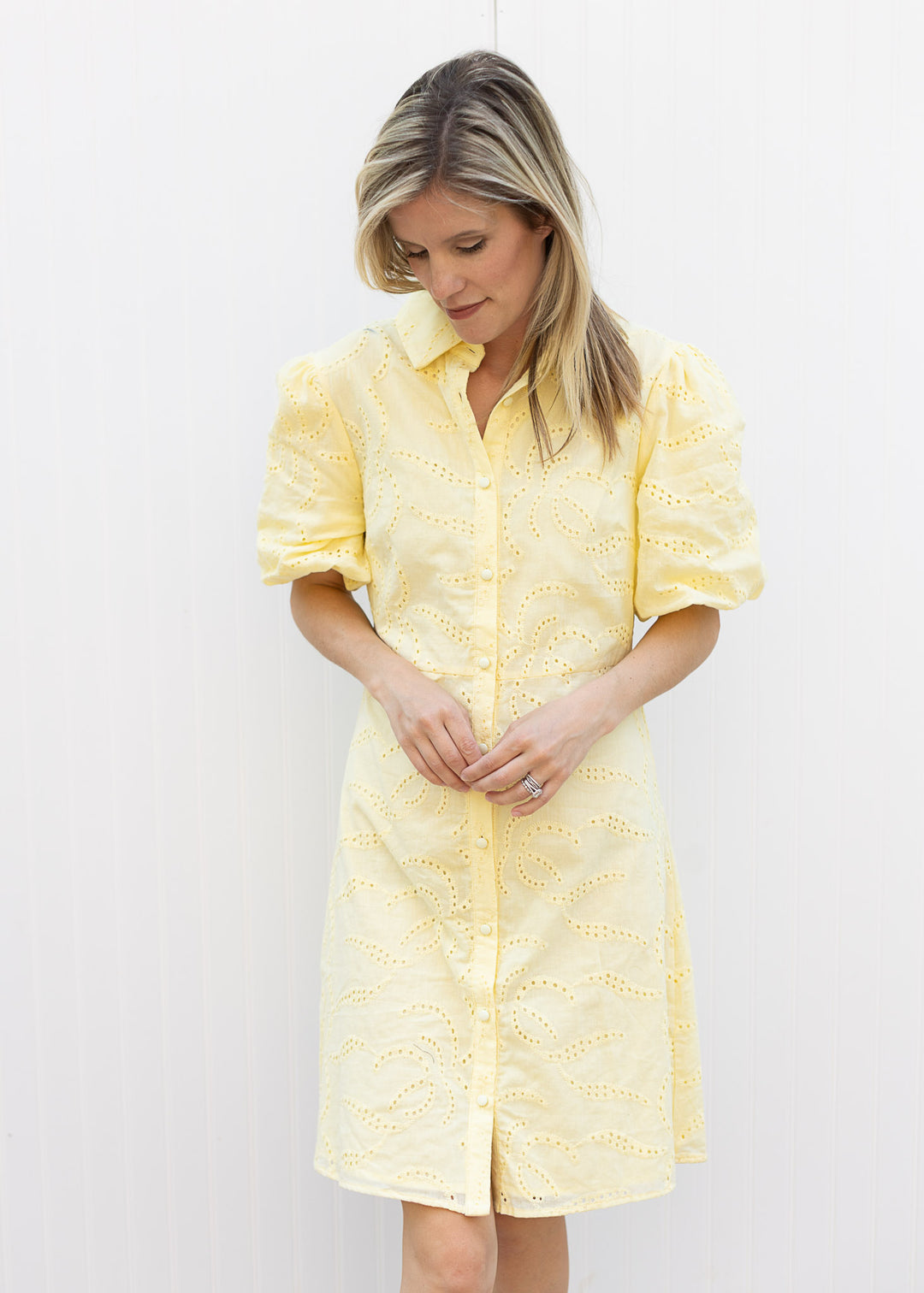 Model wearing a yellow just about the knee dress with eyelet overlay and bubble short sleeves. 