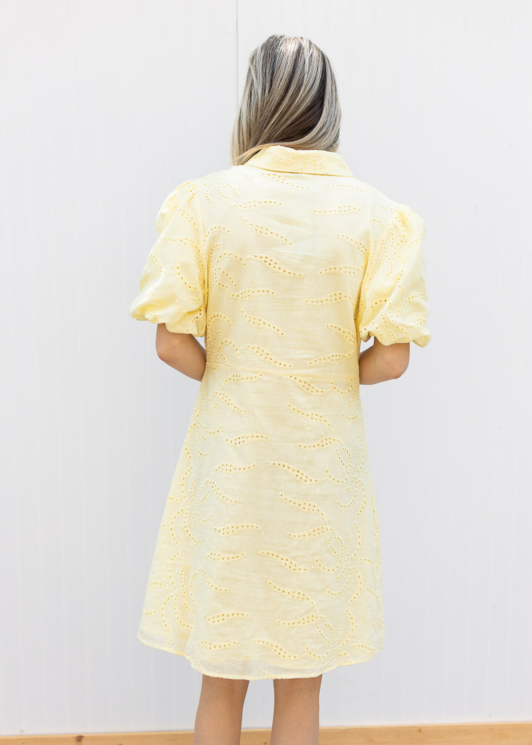Back view of Model wearing a yellow dress with eyelet overlay, collar and bubble short sleeves. 