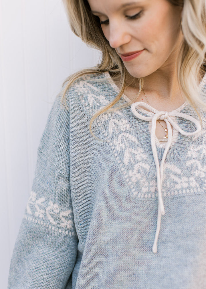 Close up of cream detailing at placket and upper arm and v-neck with a tie on a stone blue sweater. 
