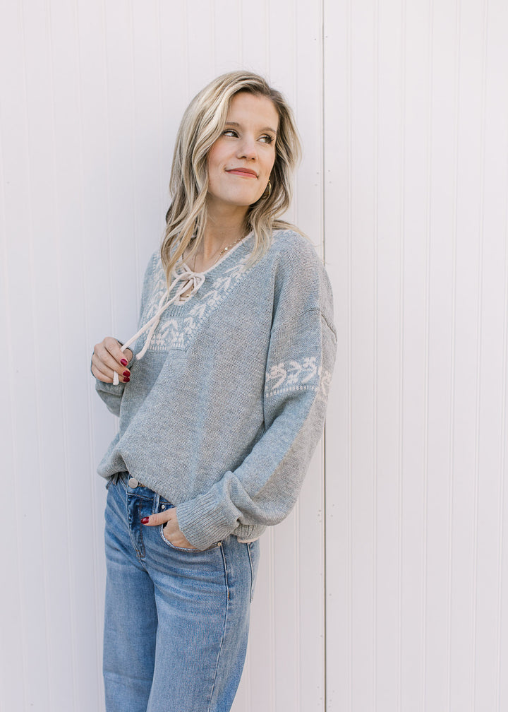 Model wearing a slightly oversized stone blue sweater with cream detailing and long sleeves. 