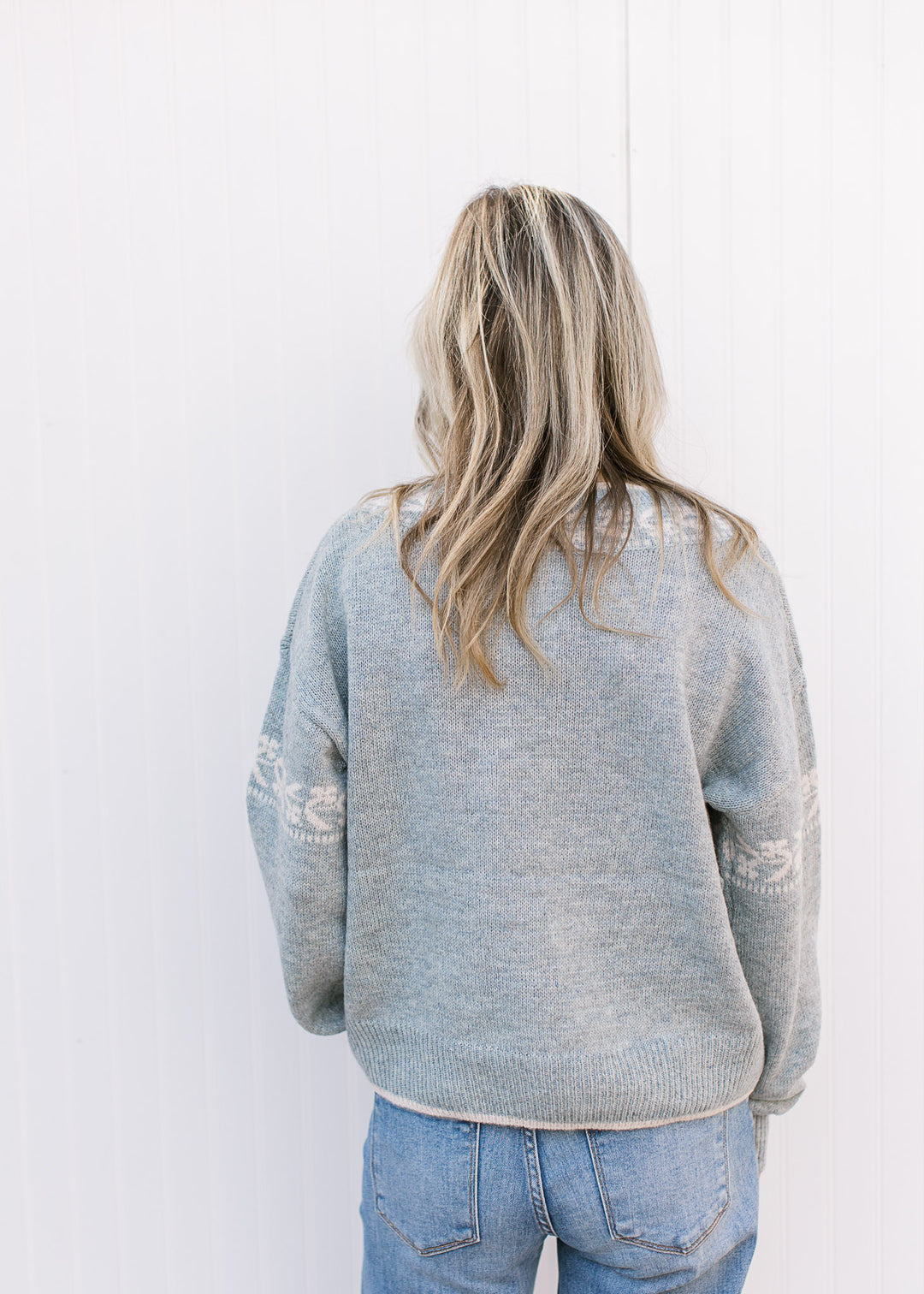 Back view of Model wearing a stone blue sweater with cream detailing, long sleeves and v-neck. 