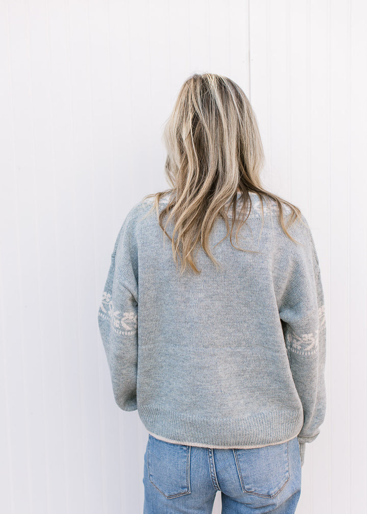 Back view of Model wearing a stone blue sweater with cream detailing, long sleeves and v-neck. 