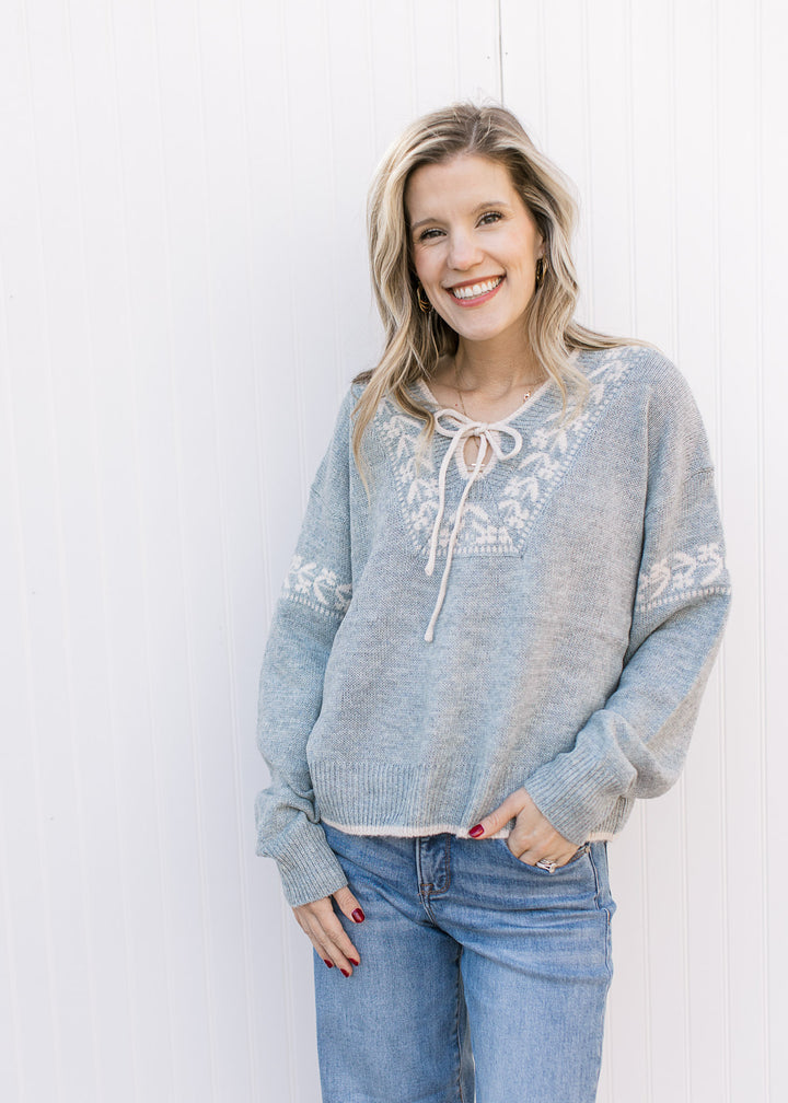 Model wearing a stone blue sweater with cream detailing, long sleeves and v-neck with a tie. 