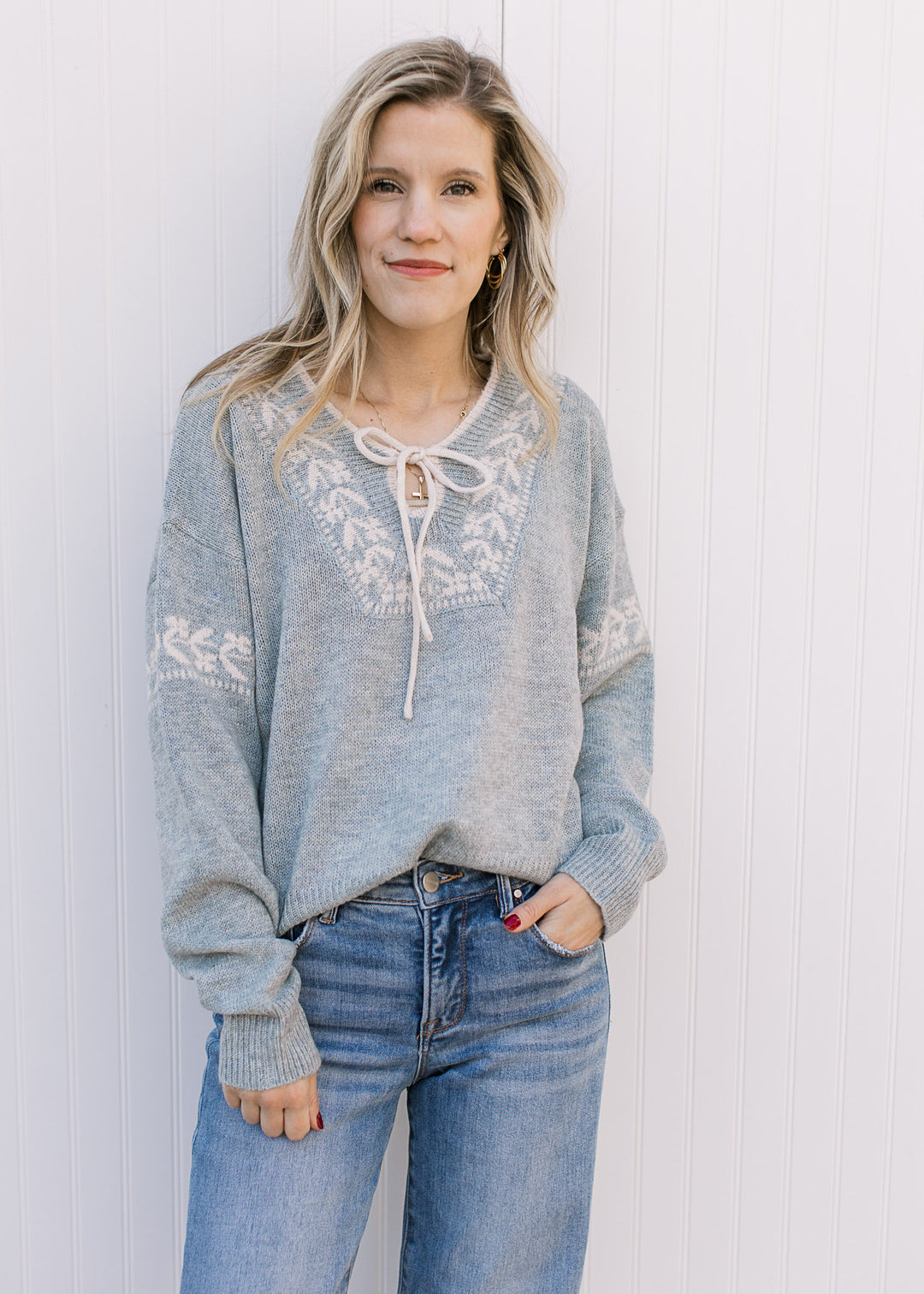 Model wearing jeans and a stone blue sweater with cream detailing, long sleeves and v-neck. 