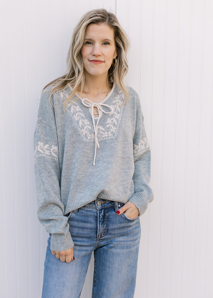 Model wearing jeans and a stone blue sweater with cream detailing, long sleeves and v-neck. 