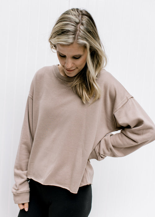 Model wearing a stone slightly cropped sweatshirt with a raw hemline, exposed hem and long sleeves.