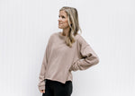Model wearing a stone polyester sweatshirt with a raw hemline, exposed hem and long sleeves.