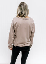 Back view of Model wearing a stone sweatshirt with a raw hemline, exposed hem and long sleeves.