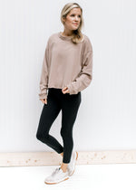Model wearing leggings and sneakers with a stone sweatshirt with a raw hemline and exposed hem. 
