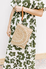 Model holding a taupe and white straw clutch bag with a wrist connection.