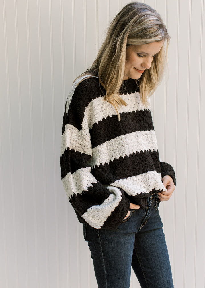Model wearing a black and white striped sweater with a knit fabric, round neck and long sleeves. 