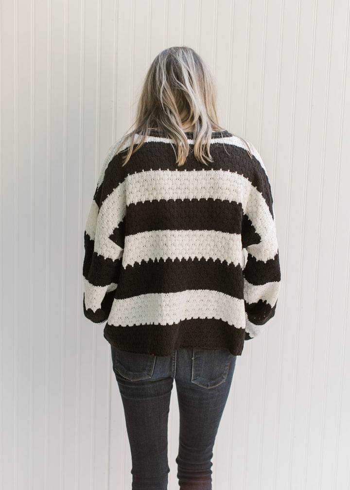 Back view of Model wearing a black and white striped sweater with a knit fabric and long sleeves. 