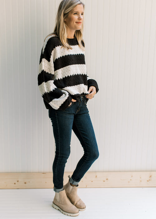 Model wearing jeans with a black and white striped sweater with a knit fabric and long sleeves. 