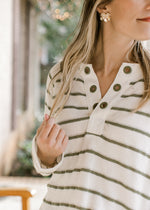 Close up of eyelets along the v-neck of a cream lightweight long sleeves top with olive stripes. 