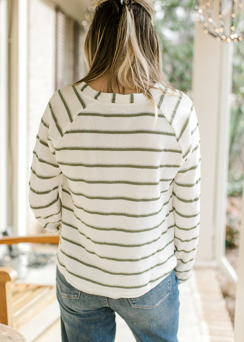 Back view of Model wearing a lightweight cream top with olive stripes, long sleeves and v-neck. 