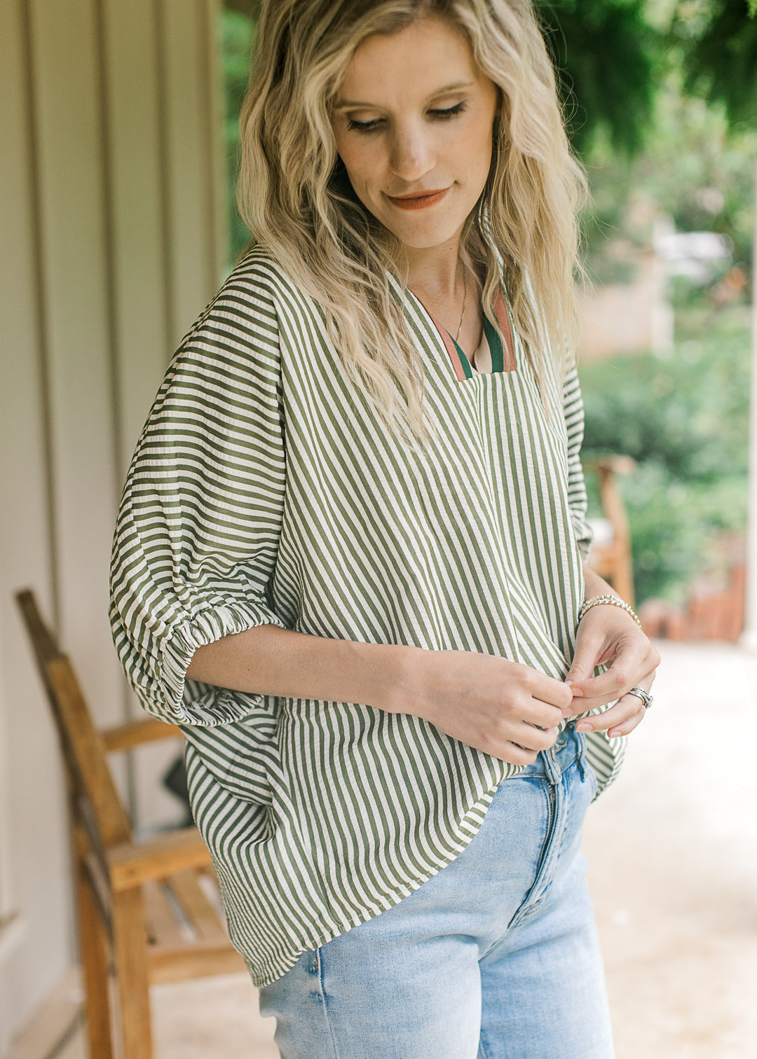 Model wearing a short sleeve olive and cream striped top with rust, navy and tan stripes at v-neck.