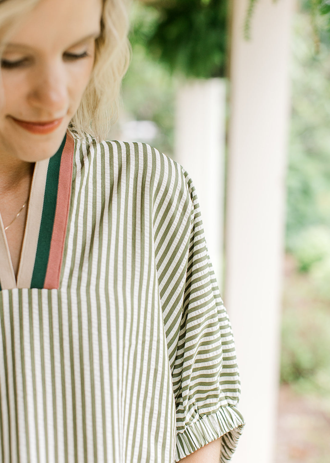 Close up of rust, navy and tan stripes at v-neck of a short sleeve olive and cream striped top.