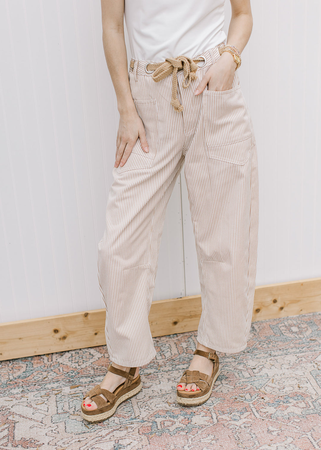 Model wearing sandals and cream barrel leg pants with tan pinstripes, woven belt and patch pockets.