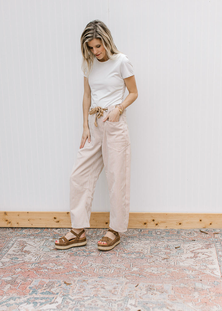 Model wearing a white top, sandals and cream barrel leg pants with tan pinstripes and a belt.